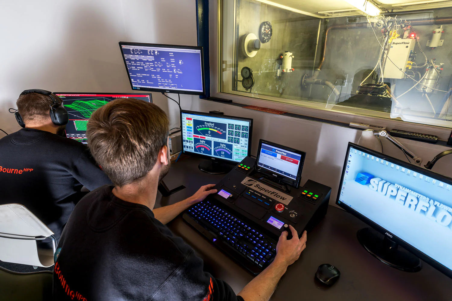 Two Bourne engineers working at a desk with multiple computer monitors in a technical setting.