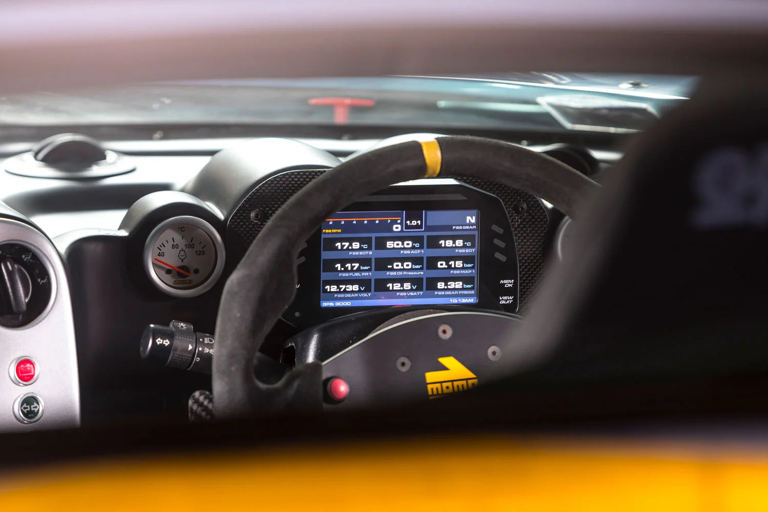 Car dashboard with digital display and steering wheel, featuring MOMO logo.