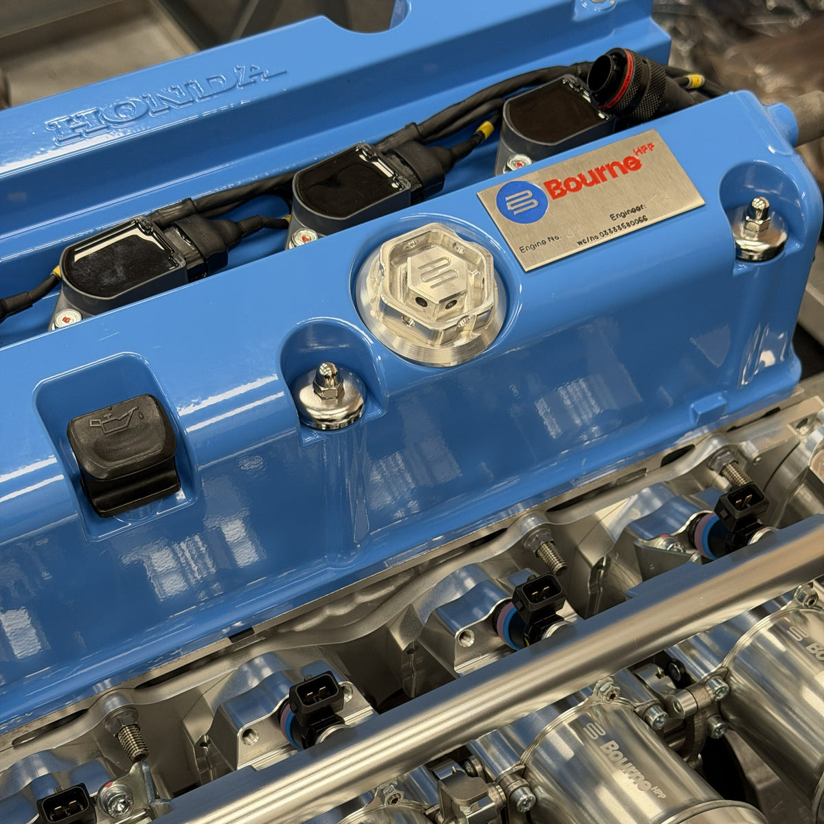Close-up of a Bourne blue Honda engine valve cover with a silver Bourne oil filler cap and various engine components visible.