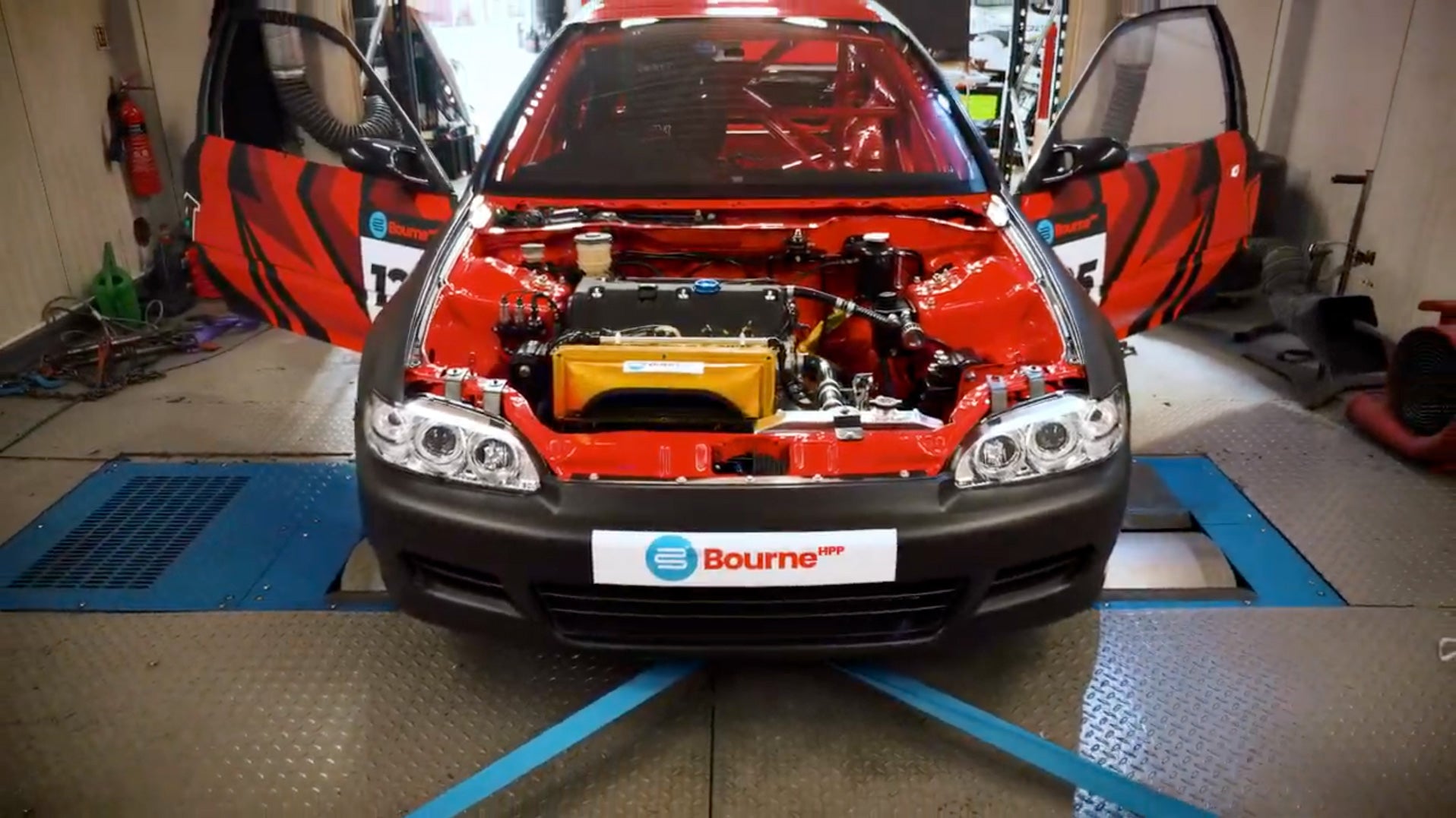 Red Honda on a rolling road with its hood open in a garage, displaying the Bourne logo.
